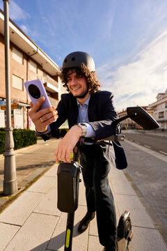 Businessman watching smartphone while riding electric scooter