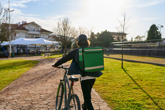 Food delivery courier pushing bicycle in urban park