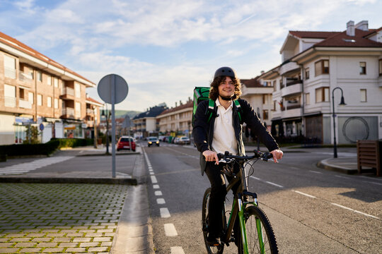 Food delivery rider smiling while cycling urban street