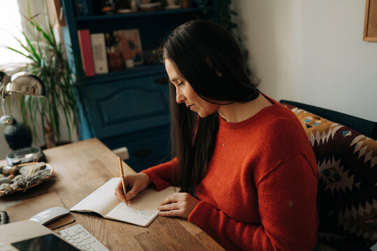 Woman Writing in Notebook at Cozy Home Workspace