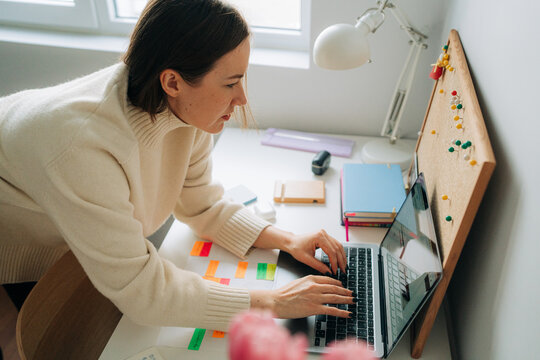 Focused Woman Typing on Laptop with Notes