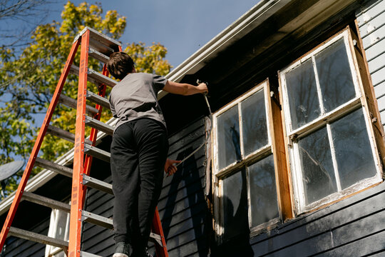 teen boy painting the exterior/siding of an old New England house 