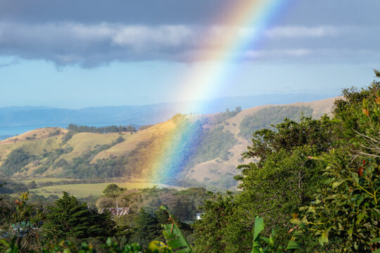 Rainbow light breaking through cloudy sky over lush hills