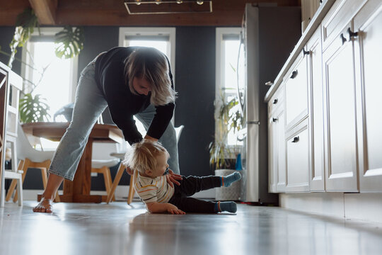 Candid mom helping toddler up on kitchen floor, real family mome