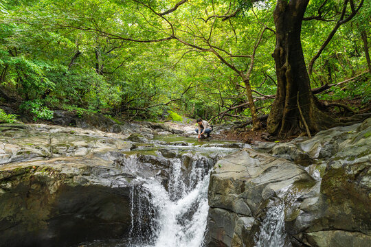 Woman scooping fresh water from jungle waterfall