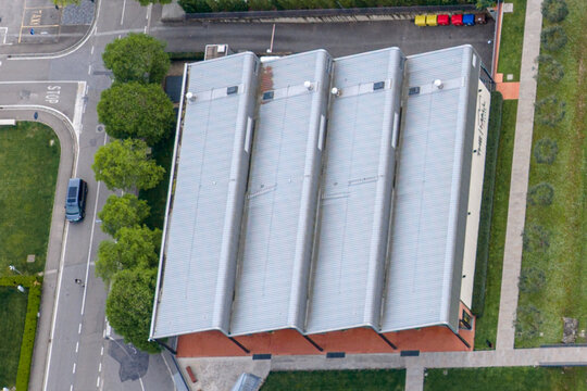 Aerial view of the modern sawtooth roof of The Mall luxury outlet building surrounded by green trees and paved roads in Reggello, Tuscany, Italy.