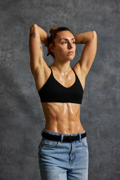 Woman poses with arms raised in front of gray background