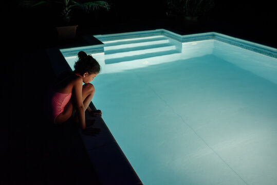 Young girl by an empty pool at night longing to jump in.