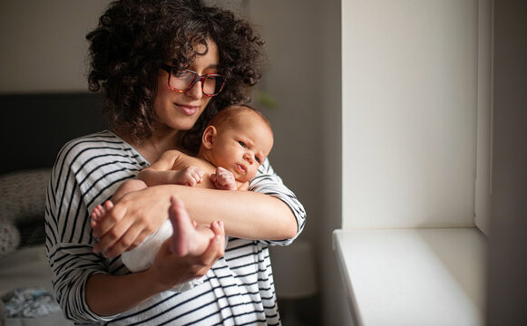 Mother Holding Newborn Baby By Window In Home