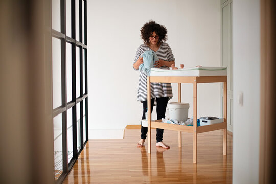 Young Mother Changing Baby on Nursery Changing Table