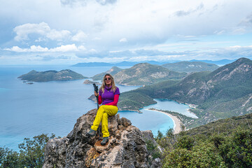 Fototapeta premium Beautiful blond woman hiker is enjoying the view of Ölüdeniz, which is a resort village on the southwest coast of Turkey, known for the blue lagoon and the wide, white Belcekız Beach. On the route of 