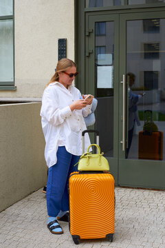 A woman with a suitcase waits outside the building, looking at her pho