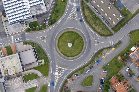 Aerial view of a modern traffic roundabout with cars driving through it, surrounded by industrial buildings with solar panels and parking lots in Reggello, Tuscany, Italy.