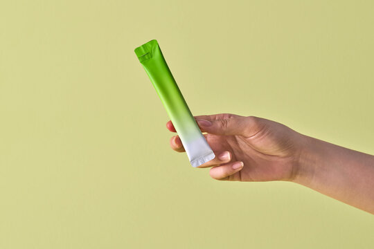 Hand Holding Green and White Supplement Packet Against yellow