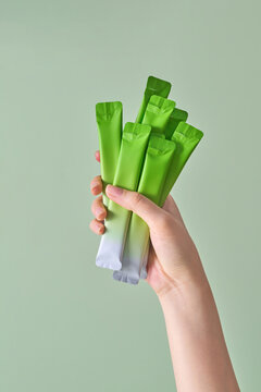 Hand Holding Green and White Snack Packets Against Yellow Backgr