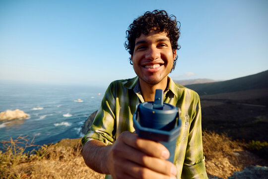 Smiling Man Holding a Water Bottle on the Pacific Coast