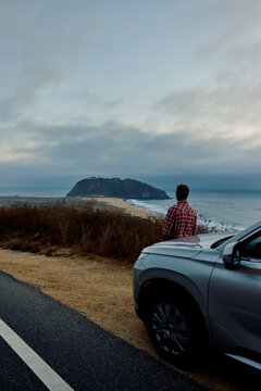 Man stands by car and looks at an island near the coast