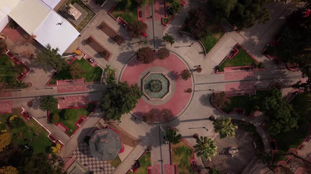 Cinematic aerial ascending shot from a water fountain in top-down view revealing the main Plaza de Armas in San Bernardo at night with bright city lights and historic architecture, 4K video.