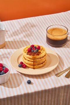 stack of waffles dripping maple syrup on table with coffee
