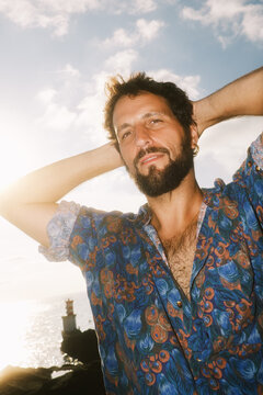 Man stands by the sea with hands behind head at sunset