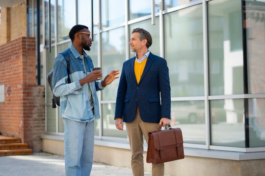 Two men talk outside a modern building