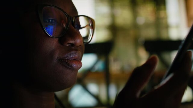 African American young adult relaxing at home with her smartphone, scrolling and texting messages. Calm indoor setting highlighting comfort and modern lifestyle habits with social media.