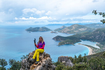 Obraz premium Beautiful blond woman hiker is enjoying the view of Ölüdeniz, which is a resort village on the southwest coast of Turkey, known for the blue lagoon and the wide, white Belcekız Beach. On the route of 