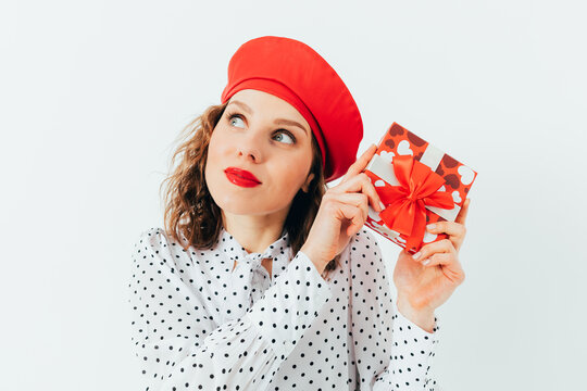 Woman holding wrapped gift, wearing red beret, smiling slightly