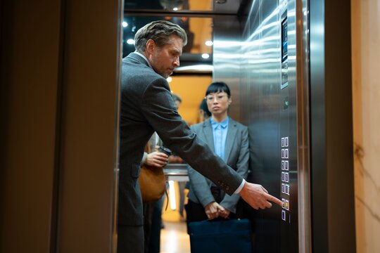 Businessman pressing elevator button while colleagues stand inside lif