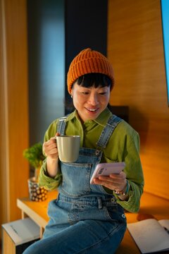 Woman enjoys drink while using phone indoors