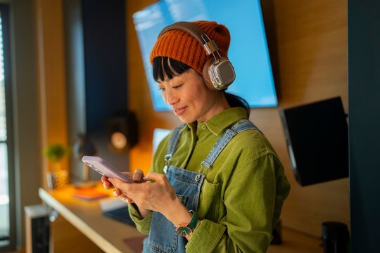 Woman using smartphone with headphones at home office