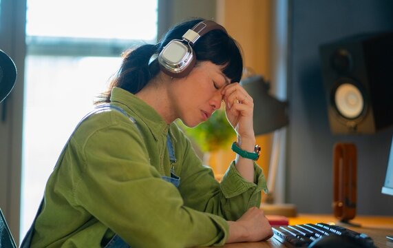Woman with headphones sits at a desk and thinks