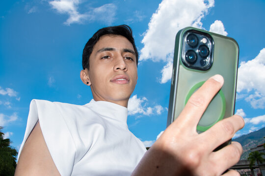 Young Man Holding Smartphone Against Blue Sky With Clouds