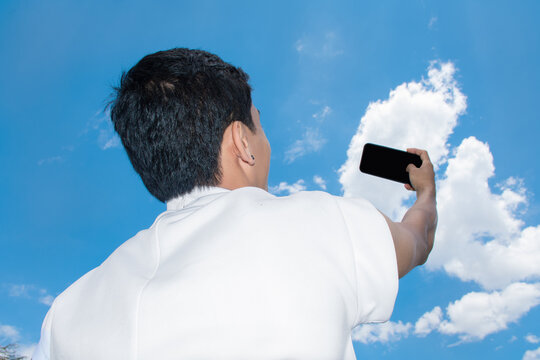 Person Takes Selfie Against a Bright Blue Sky With Clouds