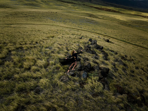 Woman in Black Flowing Dress Dancing on Rocks surrounded by Lush Grass