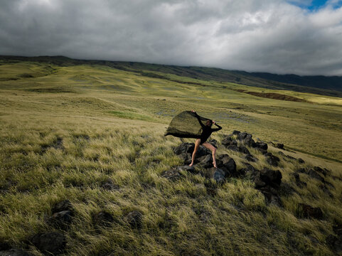 Woman in Black Flowing Dress Dancing on Rocks surrounded by Lush Grass