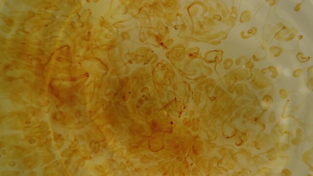 Close-up of iodine drop diffusing in water, creating dynamic abstract patterns and soft organic textures in warm colors.