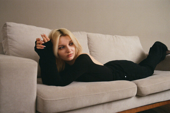Young Woman in All-Black Lying on Beige Sofa, Film Portrait