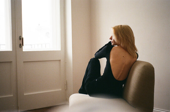 Young Woman in Backless Black Top on Armchair by Door