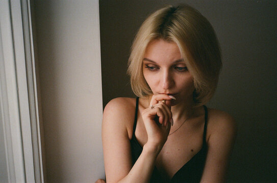 
Young Woman With Hand to Lips by Window, Moody Film Portrait