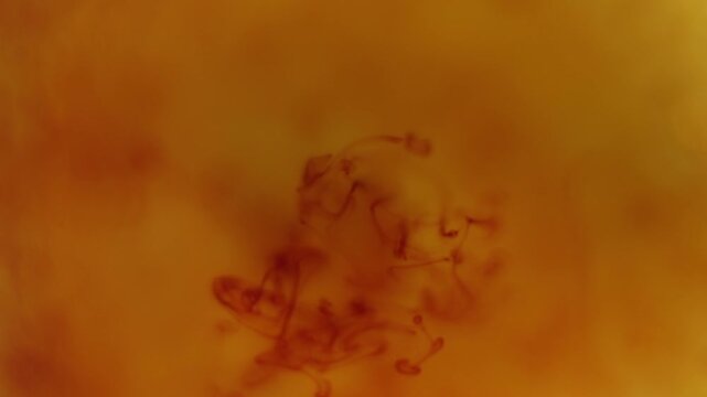 Drop of iodine dissolving in water creating abstract organic patterns and fluid motion, with warm orange tones and soft gradients.