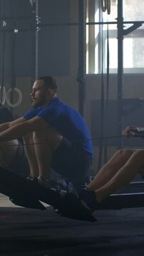 Focused men training on rowing machines in a dimly lit gym, building strength and endurance during an intense cardio workout session with functional fitness equipment