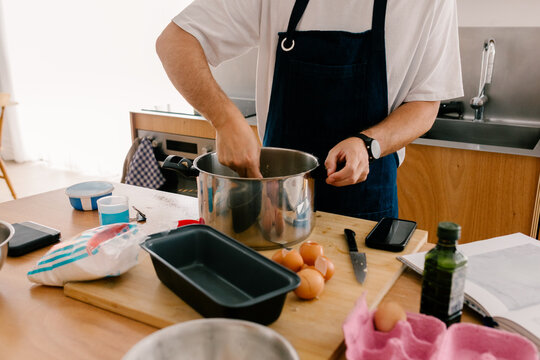 Unknown man wearing an apron baking a cake in his home kitchen