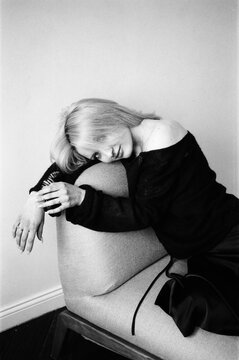 Blonde Curled Over Chair Arm in Black Outfit, B&W Portrait