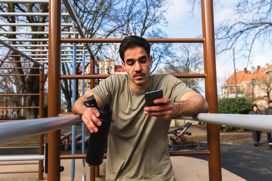 Man Checking Smartphone While Resting at Outdoor Exercise Station