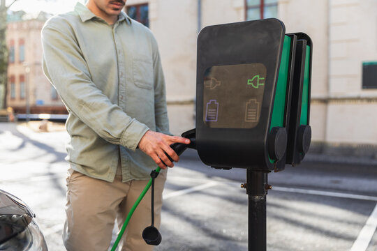 Man Plugging in Charging Cable to Electric Vehicle Station