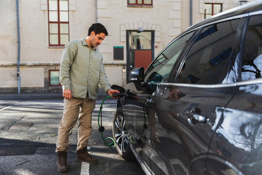 Man Connecting Charging Cable to Electric Car at Public