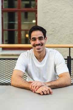 Portrait of a Smiling Male Student Sitting at a Table Indoors