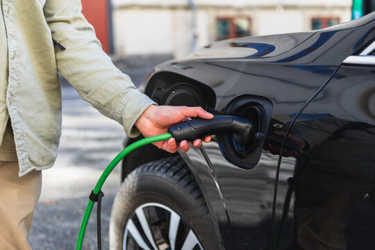 Close-up of Man Hand Plugging Green Cable into Electric Car