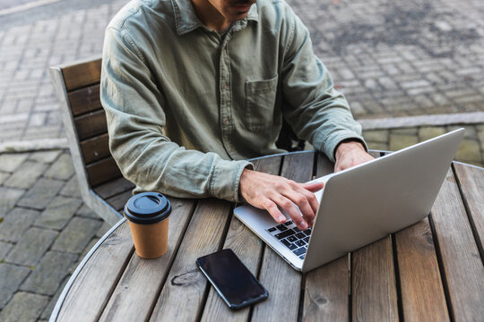 Close-up of Freelancer Typing on Laptop at a Wooden Outdoor Table